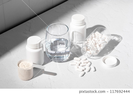 Food supplement concept. Capsules of probiotics, vitamins, white pills and a scoop of protein collagen powder.  117692444