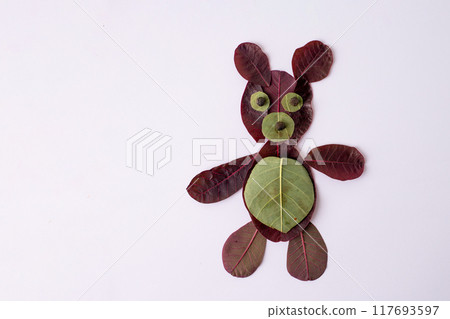Creative depiction of teddy bear made from leaves on white surface. maroon vegetable foliage for ecological art. Perfect nature craft project for kids, emphasizing natural materials and creativity., 117693597