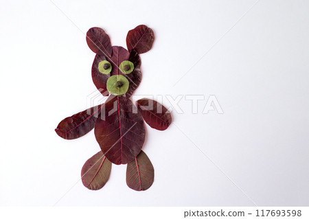Teddy bear made of leaves on white surface, ecological art. Featuring maroon vegetable foliage. Nature craft perfect for kids, blending creativity and environmental awareness 117693598