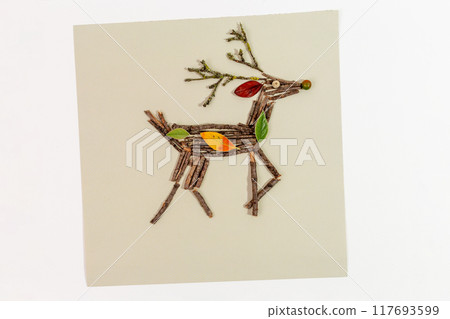 Artistic reindeer figure made of twigs and branches, with red berry eye, green berry nose, yellow and green leaves on back. Natural materials highlight creativity in festive holiday decoration 117693599