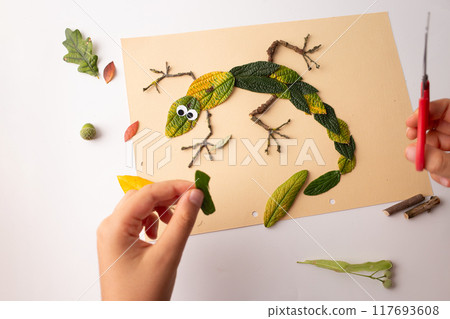 Lizard creatively depicted with natural materials on beige paper background. 117693608