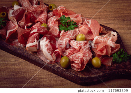 Assortment , sliced meat appetizer, prosciutto, salami and ham, with olives, on a wooden board, breakfast, top view, close-up, no people, 117693899