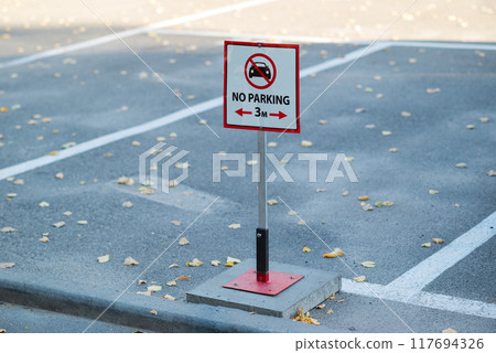 A "No Parking" sign in an empty parking lot. The pavement is partially covered with fallen leaves A "No Parking" sign in an empty parking lot. The pavement is partially covered with fallen leaves 117694326