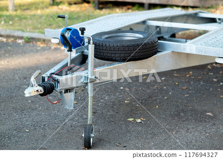 A close-up of a metal trailer hitch with a mounted spare tire and a manual winch. A close-up of a metal trailer hitch with a mounted spare tire and a manual winch. 117694327