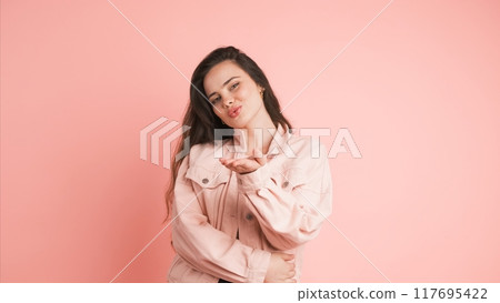 Happy woman blowing kiss and showing heart gesture in pink studio Happy woman blowing kiss and showing heart gesture in pink studio 117695422