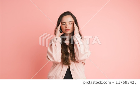 Upset woman suffering from headache in pink studio Upset woman suffering from headache in pink studio 117695423