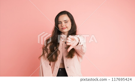 Sad young woman showing thumb down in pink studio Sad young woman showing thumb down in pink studio 117695424