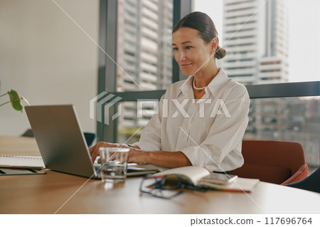 A woman is working diligently on her laptop in a contemporary and modern office space A woman is working diligently on her laptop in a contemporary and modern office space 117696764