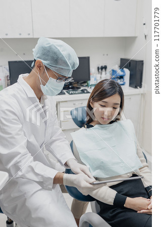 Asian male dentist sharing oral care tips to a patient 117701779