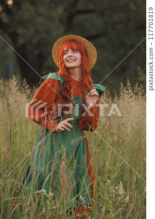 A shepherdess woman with red hair and a green dress sits in a field of flowers. 117701819
