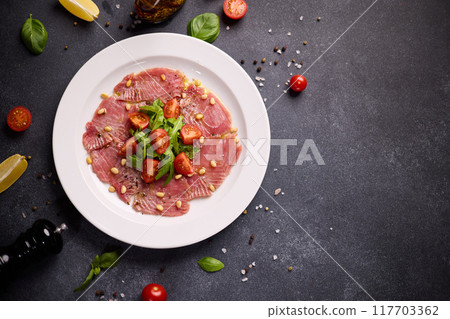 cooking tuna carpaccio - Fresh raw tuna fillet with olive oil and pine nuts on white ceramic plate 117703362