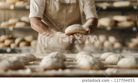 Baker preparing fresh bread loaves in a rustic bakery, surrounded by flour and dough. Artisan bread making in a traditional setting. 117704855