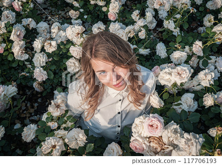 Young woman surrounded by blooming white roses enjoying nature in a beautiful garden Young woman surrounded by blooming white roses enjoying nature in a beautiful garden 117706193