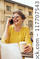 A Joyful Senior Woman Happily Enjoying Her Coffee While Engaging in Cheerful Conversation 117707543