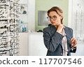 Businesswoman trying to choose glasses standing near a showcase in ophthalmic store 117707546