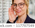 Portrait of Smiling woman in glasses in front of showcase in an optics store 117707549