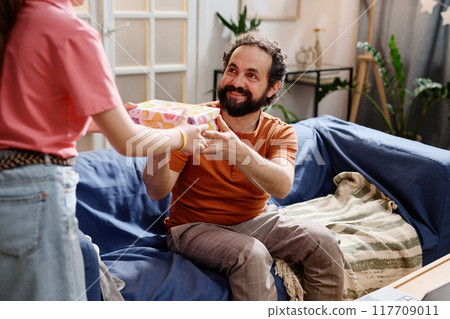 Receiving Gift Sitting on Sofa in Cozy Living Room 117709011