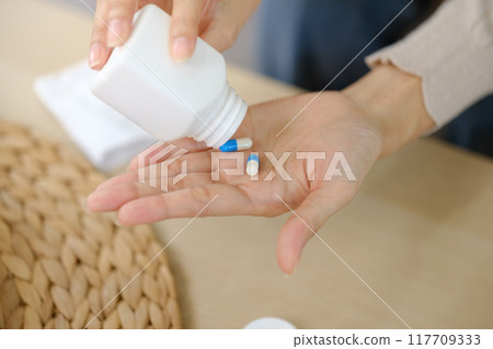 A person is taking a pill from a white bottle 117709333