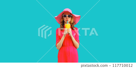 Summer portrait of beautiful young woman drinking fresh juice in hat, pink dress on blue background Summer portrait of beautiful young woman drinking fresh juice in hat, pink dress on blue background 117710012
