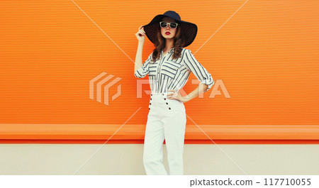 beautiful young woman posing wearing a white striped shirt, black round hat on orange background beautiful young woman posing wearing a white striped shirt, black round hat on orange background 117710055