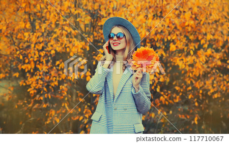 Autumn portrait of happy smiling young woman with yellow maple leaves calling on mobile phone Autumn portrait of happy smiling young woman with yellow maple leaves calling on mobile phone 117710067