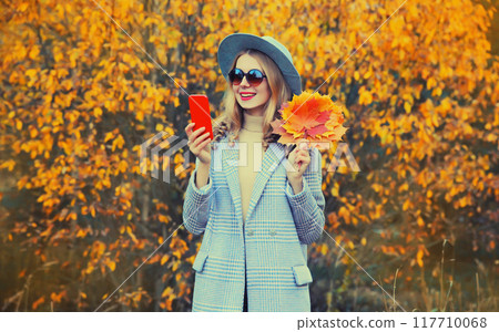 Autumn style outfit, beautiful smiling young woman model with mobile phone and yellow maple leaves Autumn style outfit, beautiful smiling young woman model with mobile phone and yellow maple leaves 117710068
