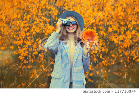 Autumn color style outfit, stylish young woman photographer with film camera and yellow maple leaves 117710074