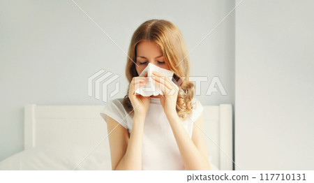 Portrait of sick upset woman sneezing blow nose using tissue Portrait of sick upset woman sneezing blow nose using tissue 117710131