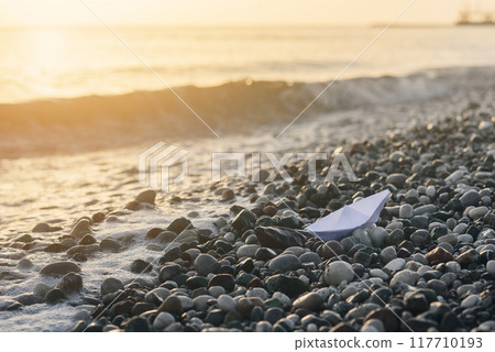 Paper boat lies on the seafront at sunrise. Paper boat lies on the seafront at sunrise. 117710193
