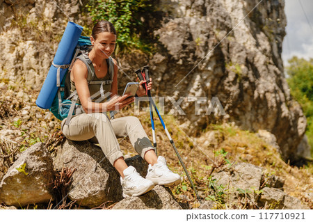 A young hiker is enjoying the beauty of nature while using a tablet on a rocky trail A young hiker is enjoying the beauty of nature while using a tablet on a rocky trail 117710921