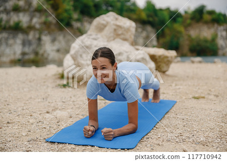 A Woman Engaged in Practicing Plank Exercise Outdoors on a Tranquil Blue Yoga Mat A Woman Engaged in Practicing Plank Exercise Outdoors on a Tranquil Blue Yoga Mat 117710942