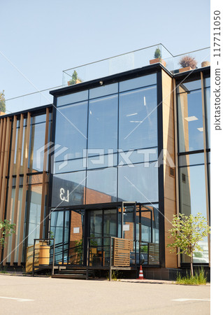 Large building facade featuring expansive glass surfaces and wooden structural elements, entrance highlighted by clean, modern design and natural light reflections Large building facade featuring expansive glass surfaces and wooden structural elements, entrance highlighted by clean, modern design and natural light reflections 117711050