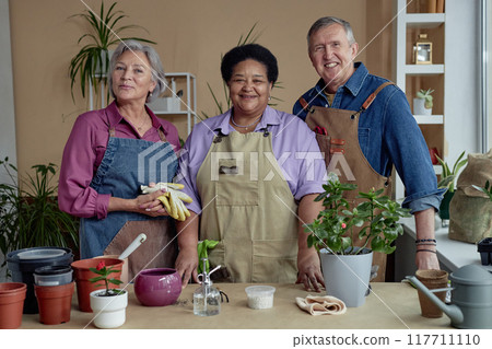 Multiethnic group of three senior people smiling at camera enjoying gardening together indoors 117711110