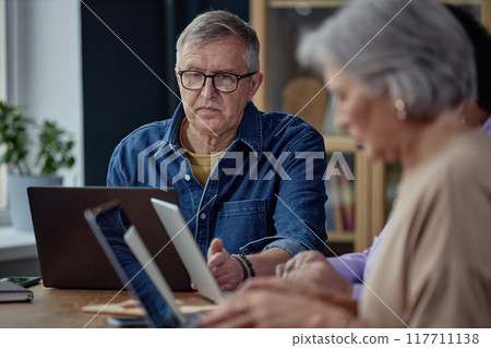 Portrait of white haired senior man using laptop and wearing glasses in computer class for adults 117711138