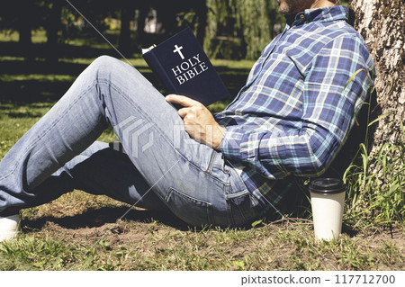 Bible study. Young man reading the Bible in the park. Christian faith concept. Bible study. Young man reading the Bible in the park. Christian faith concept. 117712700