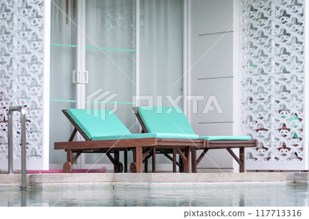 Wooden loungers with soft mattresses in pastel color by swimming pool Wooden loungers with soft mattresses in pastel color by swimming pool 117713316