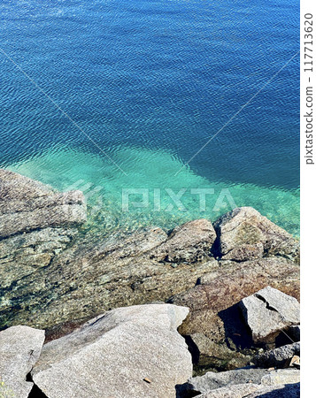 Rocky beach, deep blue-green lake, bright sun reflection. Norway 117713620