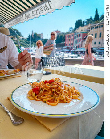 A plate of spaghetti with red sauce and on a restaurant at the beach on colorful day. Italy, Portofino. 117713763