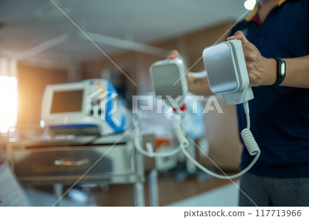 A person is holding a defibrillator in a hospital room A person is holding a defibrillator in a hospital room 117713966