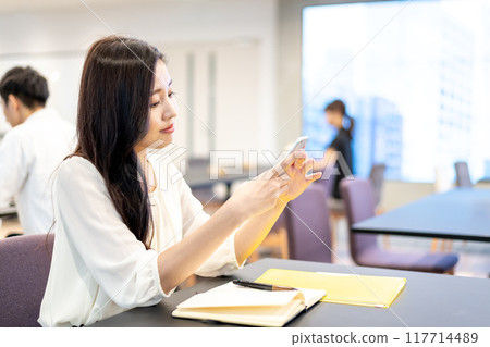 一位女士一邊在智慧型手機上收集資訊一邊思考新想法 一位女士一邊在智慧型手機上收集資訊一邊思考新想法 117714489