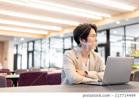 A man pondering while gazing into the distance between working on his laptop 117714494