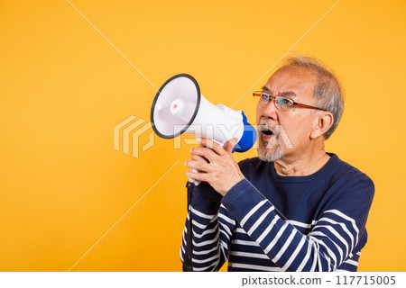 Portrait Asian old man wearing glasses screaming in megaphone studio shot isolated yellow background, happy elderly man holding a megaphone and shouts yelling announces news information Portrait Asian old man wearing glasses screaming in megaphone studio shot isolated yellow background, happy elderly man holding a megaphone and shouts yelling announces news information 117715005
