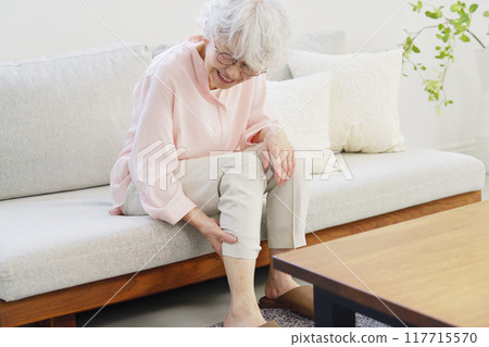 Senior woman with leg cramps in living room 117715570