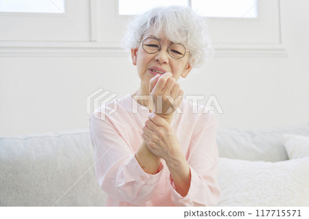 Senior woman with numb hands in living room Senior woman with numb hands in living room 117715571