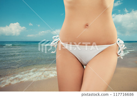 Close-up of fit bikini stomach abs. Woman with beautiful body on a tropical beach 117716686