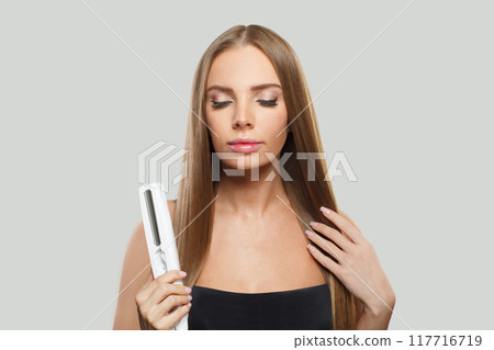 Lovely smiling woman with long straight healthy hairstyle using straightening iron  117716719
