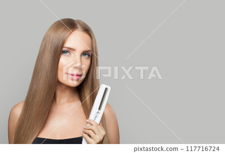 Model brunette lady with straight hair holding straightening iron Model brunette lady with straight hair holding straightening iron 117716724