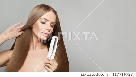 Isolated fashion model woman using hair straighteners iron on white background.  117716728