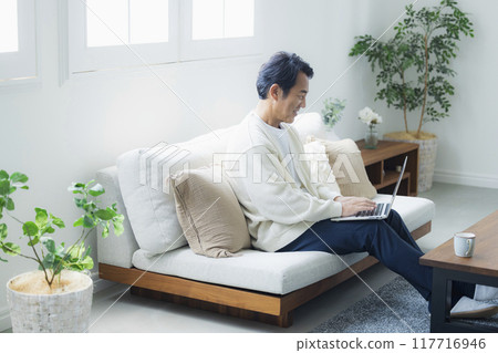 Middle-aged man using a laptop in the living room Middle-aged man using a laptop in the living room 117716946