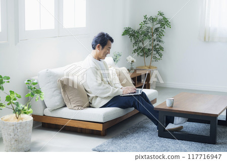 Middle-aged man using a laptop in the living room Middle-aged man using a laptop in the living room 117716947